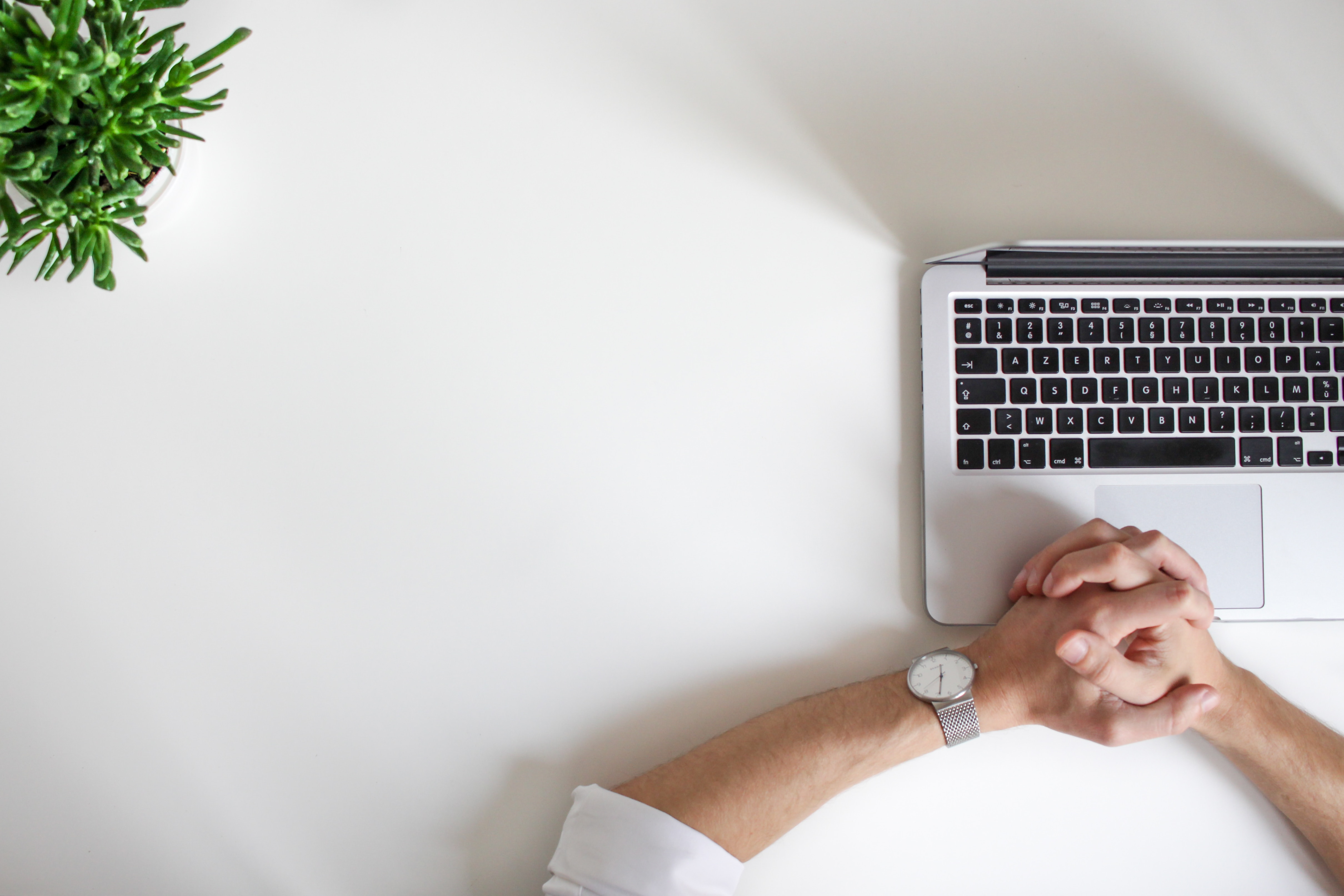 Man at desk with hands folded over laptop keyboard